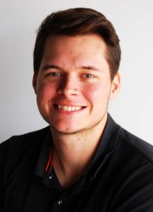 Young man with short brown hair wearing a black collared t-shirt.